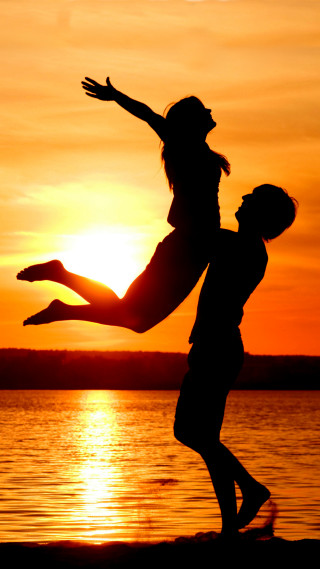 Man woman jumping sunset water - the sun setting behind them free wallpaper for mobile