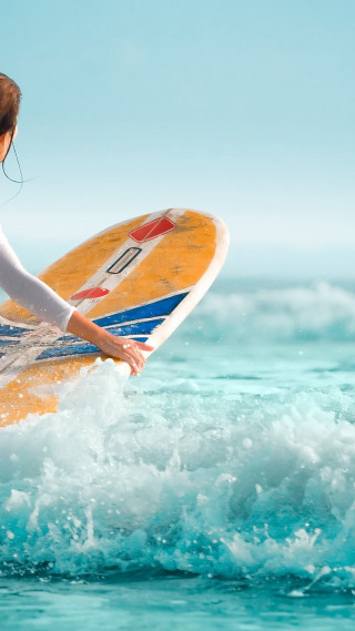 Woman holding surfboard riding wave - a surfboard free wallpaper for mobile