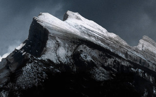 Snow covered mountain bird flying - a dark sky in the background free wallpaper