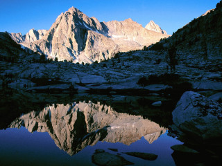 Mountain range lake foreground rocks - a clear blue sky in the background free wallpaper
