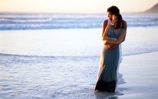 Man woman embracing beach sunset - the ocean in the background free wallpaper