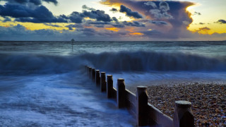 Beach waves fence sunset clouds - a light house in the distance free wallpaper for desktop