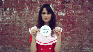 Woman holding sign dream land - a brick wall behind her free wallpaper