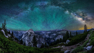 Night sky stars mountains aurora - a forest below free wallpaper