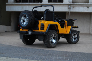 Yellow jeep parked building large - a large tire free wallpaper