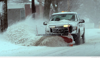 Snow plow driving snowy street - a house in the background free wallpaper