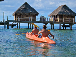 Kayak paddling towards pier thatched - the water behind them free wallpaper
