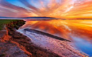 Sunset water rocky shore grassy - a sunset over a body of water free wallpaper
