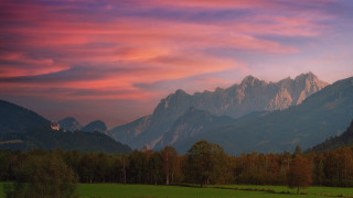 Mountain range pink sky forest 2 - a green field in the foreground free wallpaper