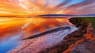 Sunset water rocky shore grassy 2 - a sunset over a body of water free wallpaper