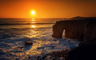 Sunset ocean rocks cloudy sky 7 - a rock formation in the foreground free wallpaper