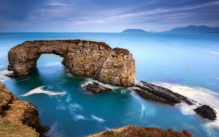 Large rock formation ocean sky - a blue ocean below free wallpaper
