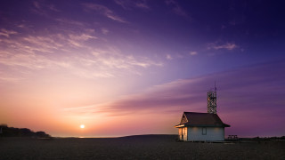 Small white building sandy beach - a sun setting behind free wallpaper