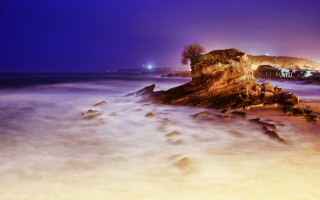 Almada negreiros beach rock formation - a city in the distance free wallpaper