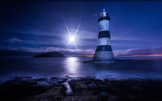 Lighthouse rocky shore night moon - a body of water below free wallpaper