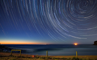 Star trail ocean night lighthouse - a lighthouse in the distance free wallpaper