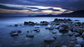 Rocky beach mountains clouds sunset - the water and a mountain in the distance free wallpaper