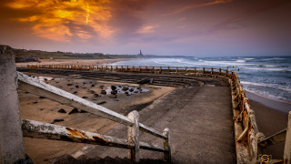 Dusk beach fence lighthouse water - a sunset in the distance free wallpaper