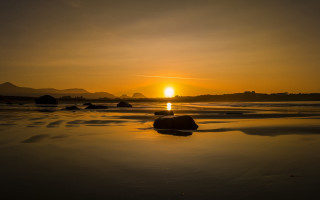 Sunset beach rocks mountain clouds - the water and a mountain in the distance free wallpaper