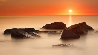 Sunset ocean rocks red sky - a bright sun in the distance free wallpaper