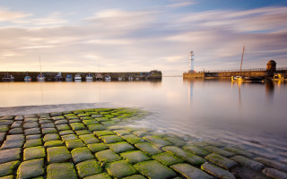 Stone walkway dock lighthouse sunset - a light house in the distance free wallpaper