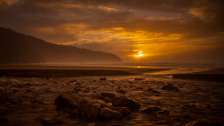 Sunset rocky beach mountain water 3 - a mountain in the background and a body of water free wallpaper