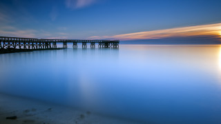 Pier sunset calm water reflection - the sun in the distance free wallpaper