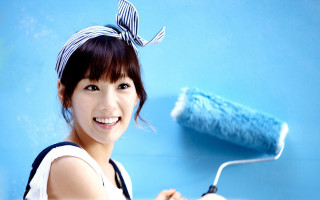 Cheerful woman painting blue wall - a blue wall free wallpaper