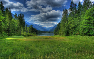 Grassy field lake mountains clouds - a lake in the middle of it free wallpaper for desktop