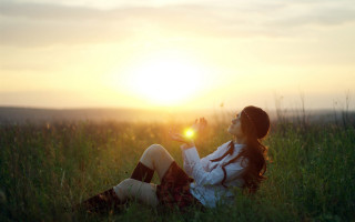 Woman sitting field sunset flare - the sun shining behind her free wallpaper