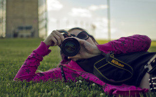 Woman grass camera lens building - her hand and a building in the background free wallpaper