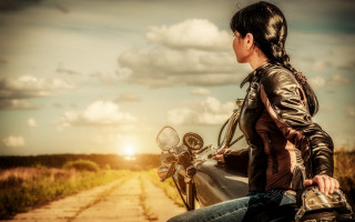 Woman motorcycle dirt road sunset - the sun setting behind her free wallpaper