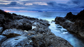 Rocky beach sunset cloudy sky - a small island in the distance free wallpaper
