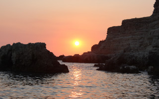 Sunset water rocks boat mountain - the foreground and a boat in the distance free wallpaper