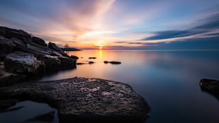 Sunset water rocks clouds horizon 2 - a sunset over a body of water free wallpaper