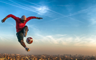 Man jumping soccerball city background - his hand and a city in the background free wallpaper