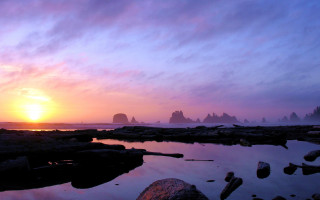 Sunset rocky beach city lights 3 - a large rock formation in the background free wallpaper