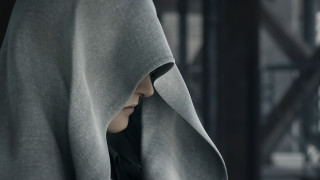 Woman hooded cloak looking distance - a blurry background of a building free wallpaper