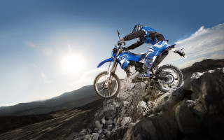 Man riding dirtbike rocky hill - cloud and sun free wallpaper