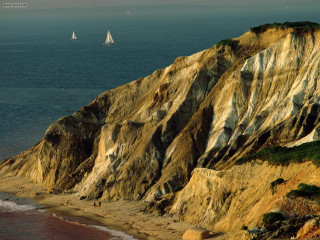 Rocky cliff sailboat distance water - a sandy shore free wallpaper